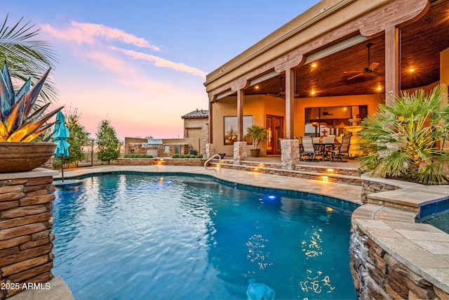 pool at dusk with a patio area, pool water feature, and ceiling fan