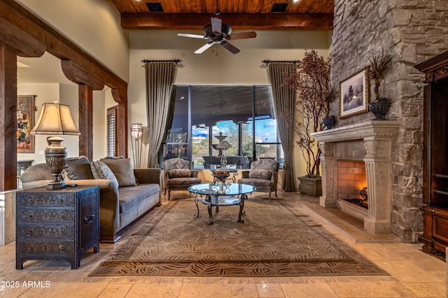 living room with a fireplace, beamed ceiling, a high ceiling, ceiling fan, and wood ceiling