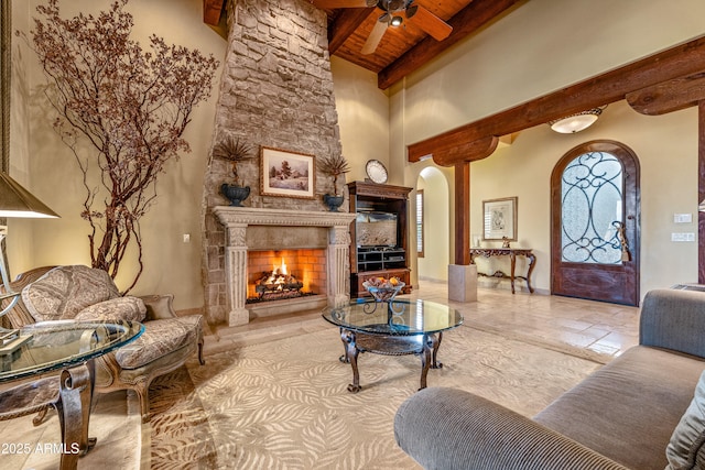 sitting room featuring beamed ceiling, a large fireplace, a high ceiling, ceiling fan, and wood ceiling