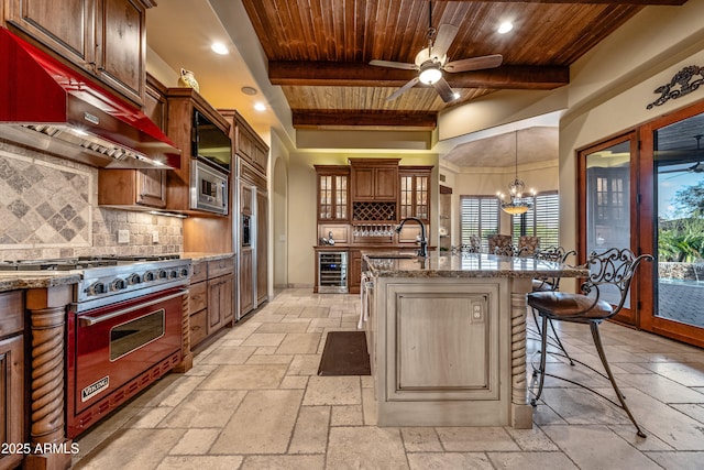 kitchen featuring wine cooler, a kitchen bar, a kitchen island with sink, built in appliances, and wood ceiling