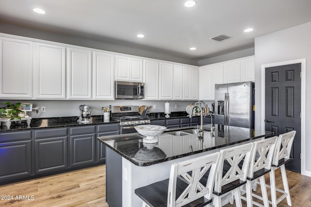 kitchen with appliances with stainless steel finishes, sink, light hardwood / wood-style flooring, white cabinets, and an island with sink