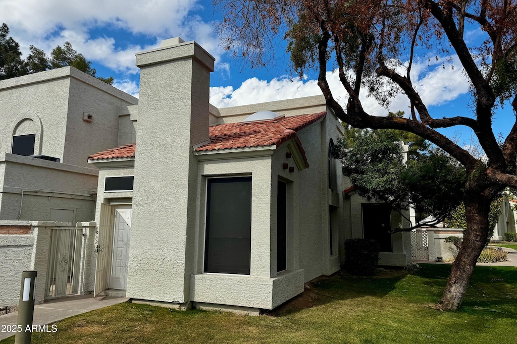 rear view of house featuring stucco siding, a chimney, a lawn, and a tiled roof