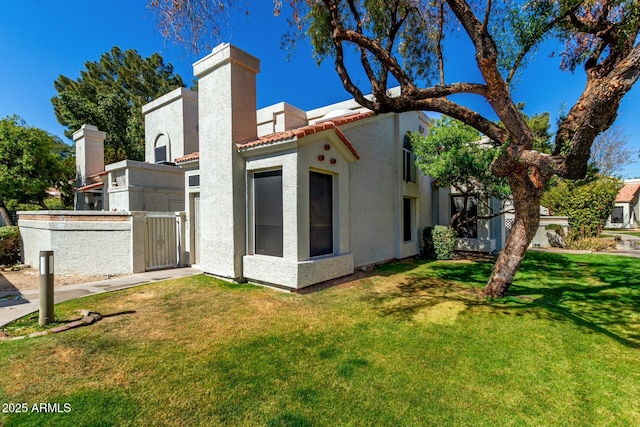 rear view of house featuring a yard, a chimney, a tile roof, and stucco siding