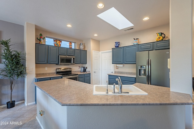 kitchen with a skylight, sink, stainless steel appliances, an island with sink, and light tile patterned floors