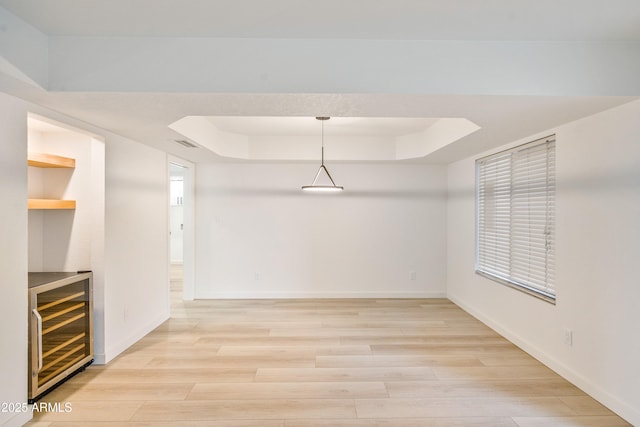 interior space featuring wine cooler, light hardwood / wood-style flooring, and a raised ceiling