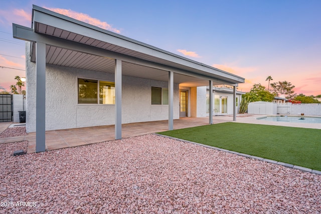 back house at dusk with a fenced in pool, a patio, and a lawn