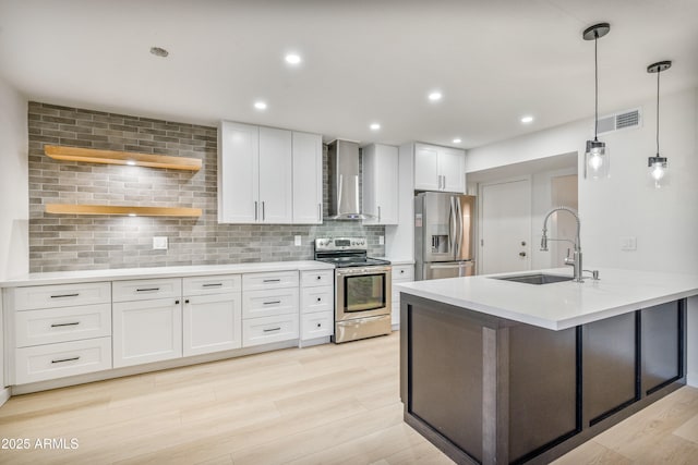 kitchen with appliances with stainless steel finishes, decorative light fixtures, sink, white cabinets, and wall chimney range hood