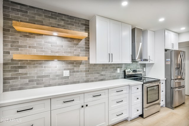 kitchen with appliances with stainless steel finishes, white cabinets, decorative backsplash, wall chimney range hood, and light wood-type flooring