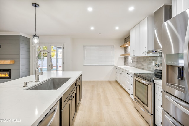 kitchen with appliances with stainless steel finishes, sink, white cabinets, hanging light fixtures, and light stone counters