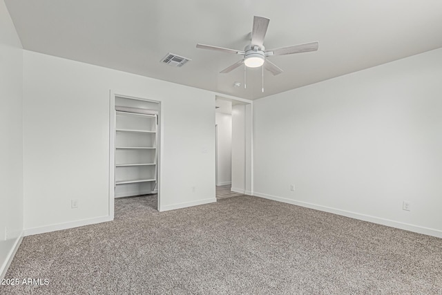 unfurnished bedroom with carpet, visible vents, a ceiling fan, a walk in closet, and baseboards
