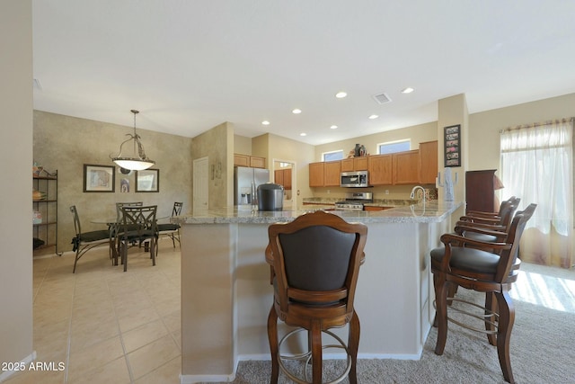 kitchen featuring a breakfast bar area, light stone counters, kitchen peninsula, pendant lighting, and stainless steel appliances