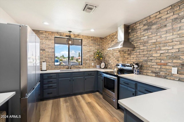 kitchen featuring brick wall, appliances with stainless steel finishes, wall chimney exhaust hood, and light hardwood / wood-style floors