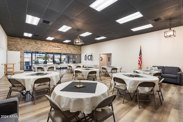 dining area with brick wall, a paneled ceiling, an inviting chandelier, and hardwood / wood-style floors