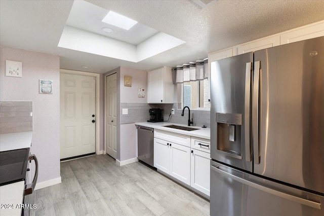 kitchen with light hardwood / wood-style flooring, appliances with stainless steel finishes, tasteful backsplash, sink, and white cabinetry