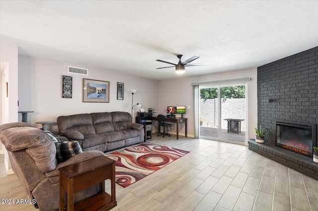 living room with a textured ceiling, ceiling fan, a brick fireplace, and light hardwood / wood-style floors