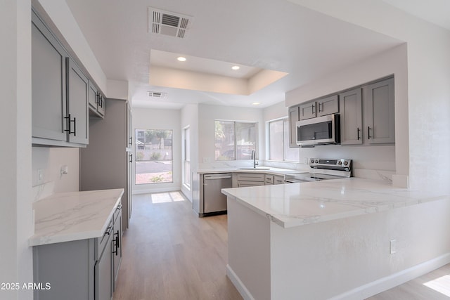 101 N 7th St Unit 168, Phoenix, AZ 85034 - kitchen with stainless steel appliances, gray cabinets, light wood-type flooring, light stone countertops, and a peninsula