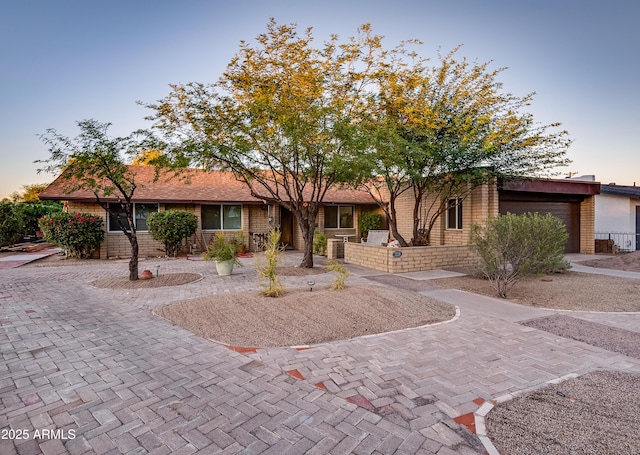 ranch-style home featuring decorative driveway, brick siding, and an attached garage