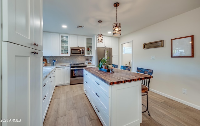 7226 E Virginia Ave, Scottsdale, AZ 85257 - kitchen featuring appliances with stainless steel finishes, butcher block countertops, a kitchen bar, decorative backsplash, and light wood-style flooring