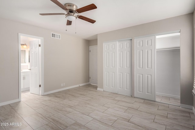 unfurnished bedroom featuring multiple closets, ensuite bathroom, and ceiling fan