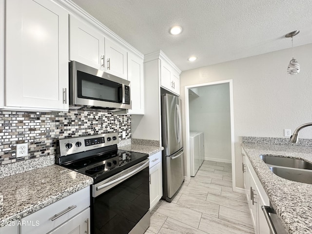 kitchen featuring appliances with stainless steel finishes, washer and dryer, sink, white cabinets, and light stone counters