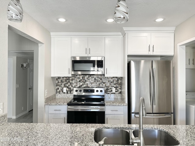 kitchen featuring appliances with stainless steel finishes, white cabinets, light stone counters, and decorative backsplash