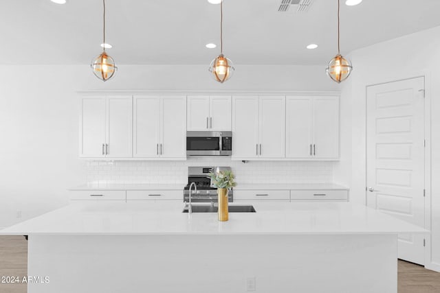 kitchen with a kitchen island with sink, sink, pendant lighting, and white cabinetry