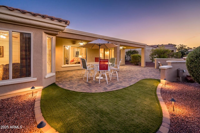 patio terrace at dusk with ceiling fan and a lawn