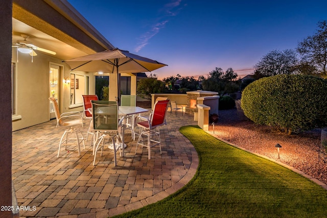 patio terrace at dusk with ceiling fan and an outdoor kitchen