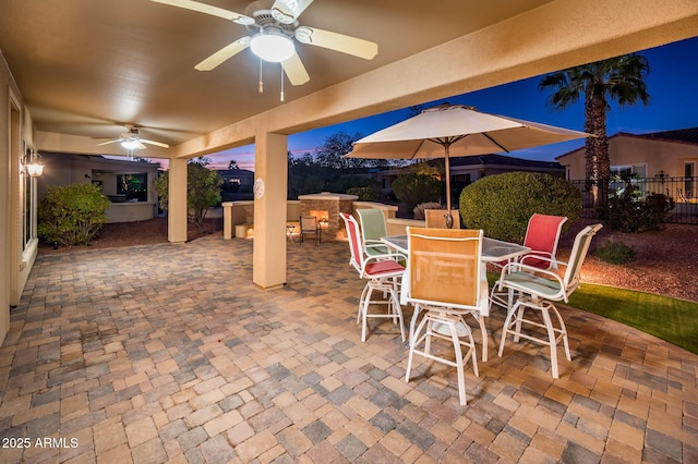 patio terrace at dusk featuring ceiling fan, exterior bar, and area for grilling