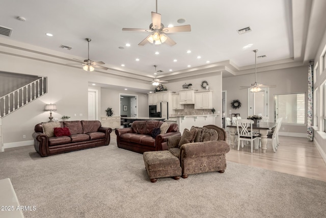 living room featuring a tray ceiling, stairway, visible vents, and baseboards