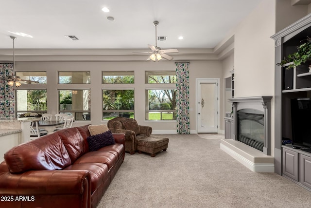 living area with a ceiling fan, a glass covered fireplace, visible vents, and light colored carpet