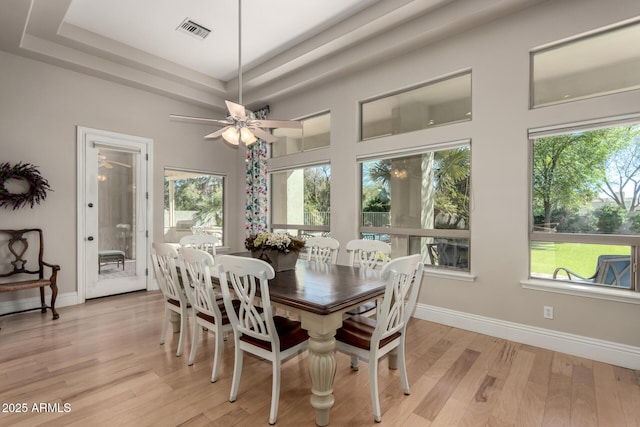 dining room with baseboards, a raised ceiling, visible vents, and light wood-style floors