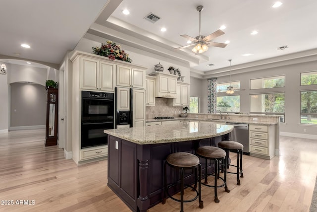 kitchen with dobule oven black, visible vents, a center island, cream cabinetry, and stainless steel dishwasher