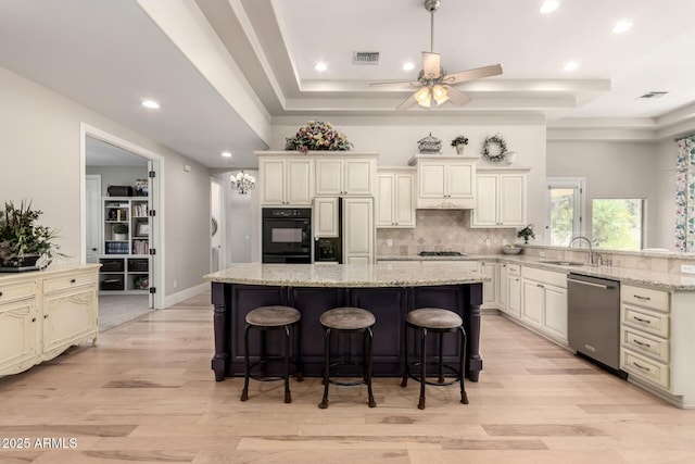 kitchen with dishwasher, light stone counters, a center island, a tray ceiling, and a sink