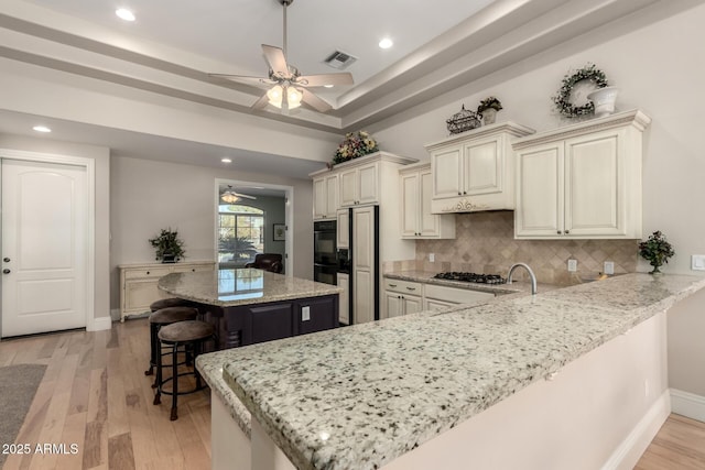 kitchen featuring light stone counters, a peninsula, visible vents, a kitchen breakfast bar, and a center island