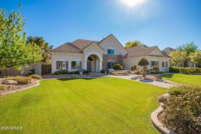 view of front of house with stucco siding, a front yard, fence, stone siding, and a tiled roof