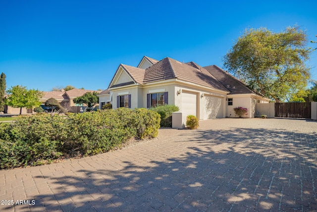 view of front facade with decorative driveway, a tile roof, stucco siding, fence, and a garage