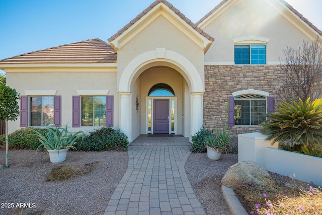 entrance to property with stone siding, a tile roof, and stucco siding