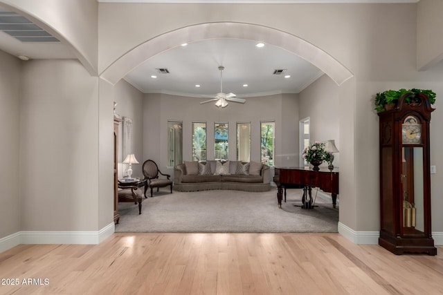 living area featuring arched walkways, light wood-style flooring, a ceiling fan, visible vents, and baseboards