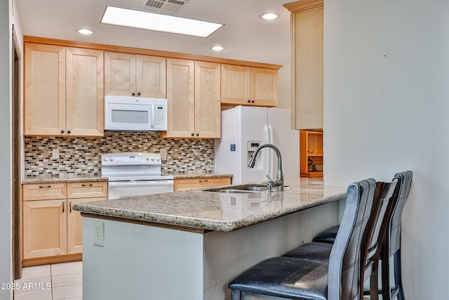 kitchen with white appliances, light brown cabinetry, and kitchen peninsula