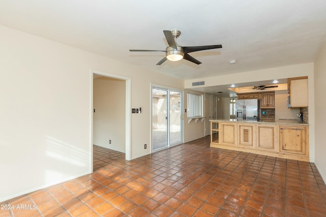 interior space featuring ceiling fan, stainless steel fridge, light brown cabinets, and tasteful backsplash