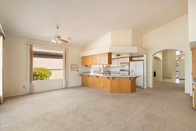 kitchen featuring light carpet, white appliances, a breakfast bar, a peninsula, and light countertops