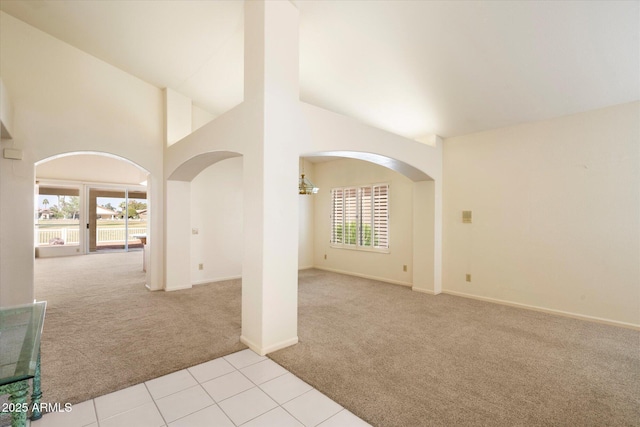 carpeted empty room featuring high vaulted ceiling, arched walkways, tile patterned flooring, and baseboards