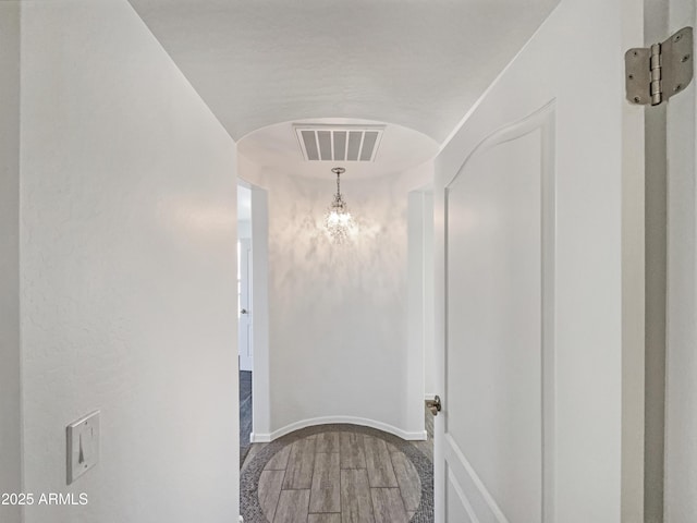 hallway featuring arched walkways, visible vents, an inviting chandelier, wood finished floors, and baseboards