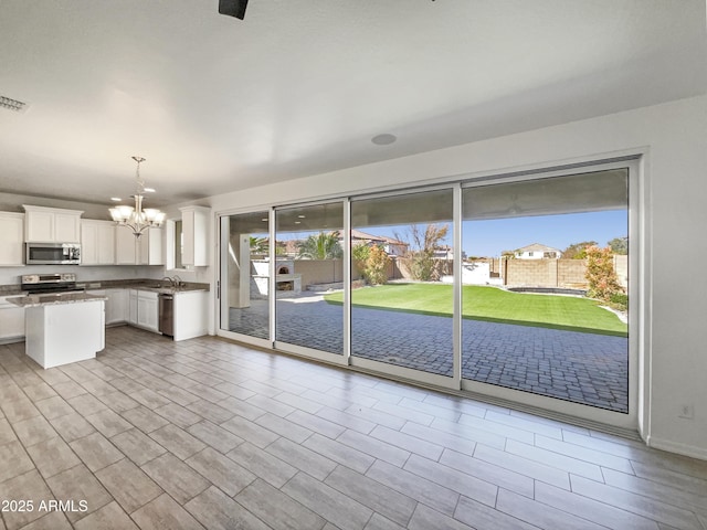 kitchen with stone countertops, a notable chandelier, stainless steel appliances, white cabinetry, and hanging light fixtures