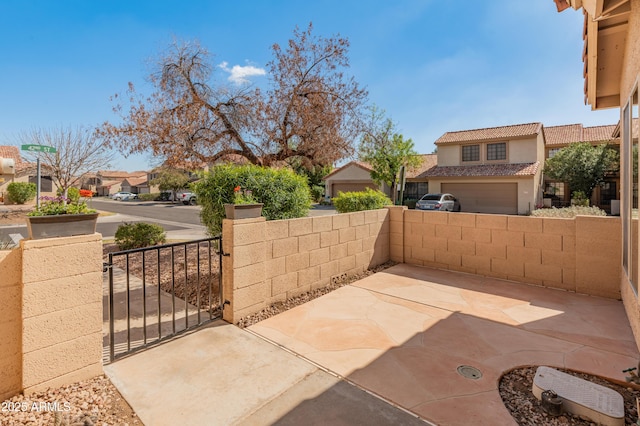 view of patio featuring an attached garage, a fenced front yard, a residential view, driveway, and a gate