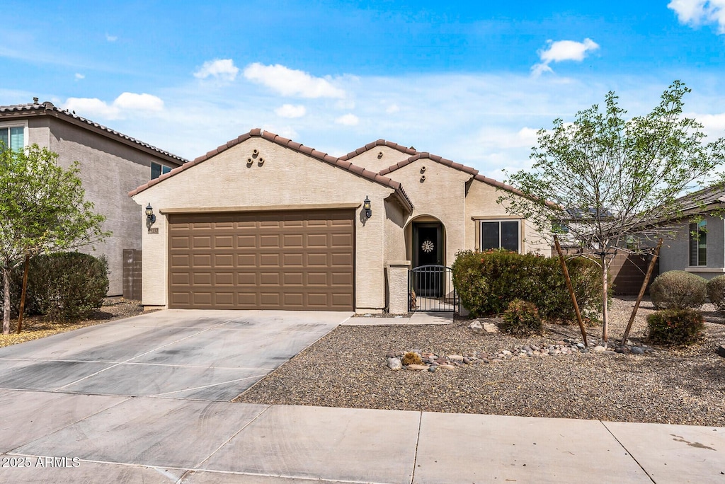 mediterranean / spanish home with an attached garage, driveway, a tiled roof, a gate, and stucco siding