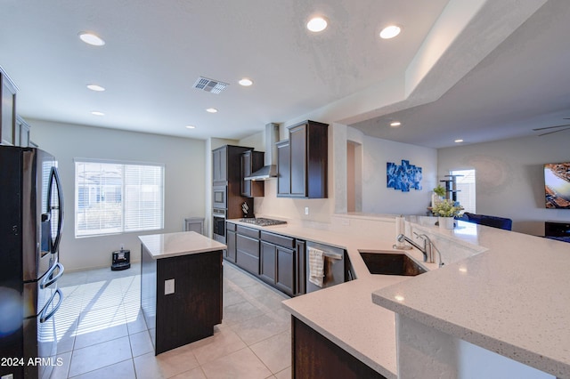 kitchen with a center island, a kitchen breakfast bar, sink, wall chimney exhaust hood, and appliances with stainless steel finishes