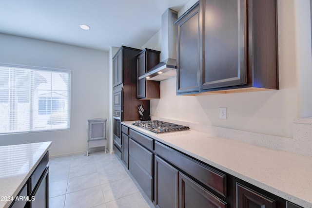 kitchen featuring wall chimney exhaust hood, light stone counters, light tile patterned floors, and appliances with stainless steel finishes