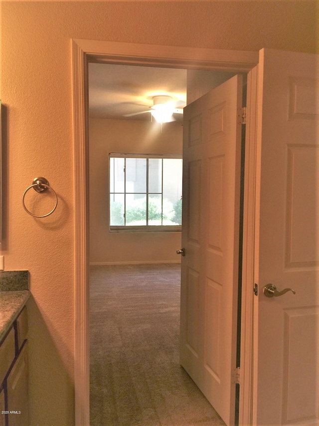 hall with carpet flooring, a textured wall, and baseboards